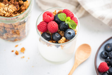 Yogurt with berries and granola in jar on white table. Clean eating, dieting, healthy food concept