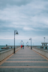 Fototapeta premium A couple taking a walk on a bridge in the sea. Winter autumn season.