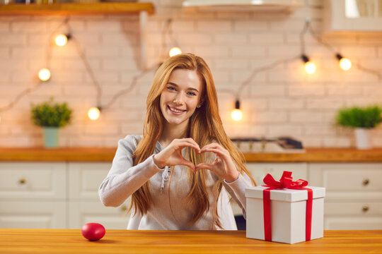 Smiling woman shows heart in front of the camera, expressing love to her lover during a video call.