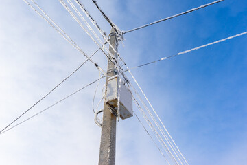 a pole with electric wires covered with snow and frost. frozen wires on the street.