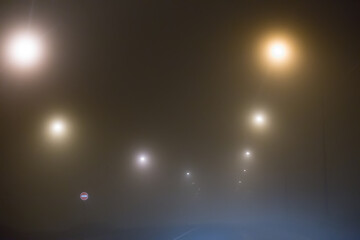 Thick fog on a country road lit by lamps