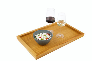 Drewniana taca z lampkami wina czerwonym i białym obok w miseczce kostki sera z warzywami, całośc na białym tle © JDziedzic