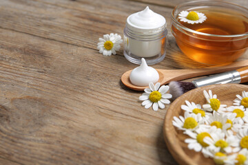 Composition with chamomile flowers and cosmetic products on wooden table. Space for text