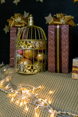 Christmas decorations. Golden cage with various balls on the background of a black wall with golden stars.