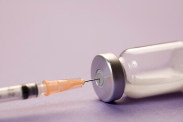 medical syringe cannula with vaccine vial, lilac background. macro