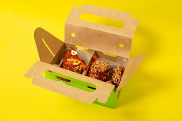 Chinese takeaway chicken with tomatoes, in a cardboard box photographed on a yellow background