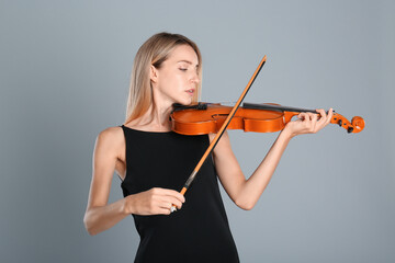 Beautiful woman playing violin on grey background