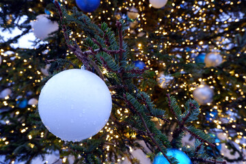 Close up view on wet misted matte white christmas ball with water drops on christmas tree branch with lights selective focus on bokeh background