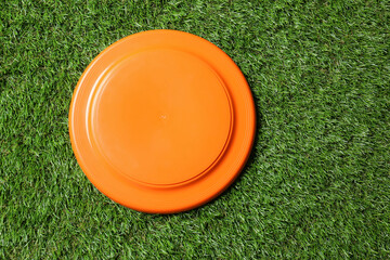 Orange plastic frisbee disk on green grass, top view - obrazy, fototapety, plakaty