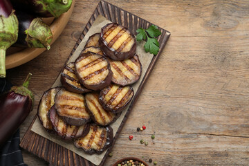 Delicious grilled eggplant slices on wooden table, flat lay. Space for text