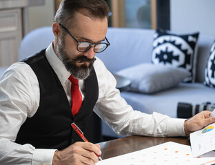 Portrait of concentrated bearded businessman in eyeglasses and formal wear looking at planner while working in the office