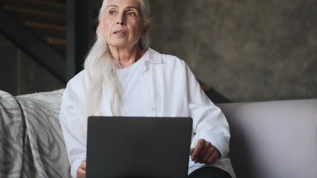 Serious senior woman using laptop computer indoors at home