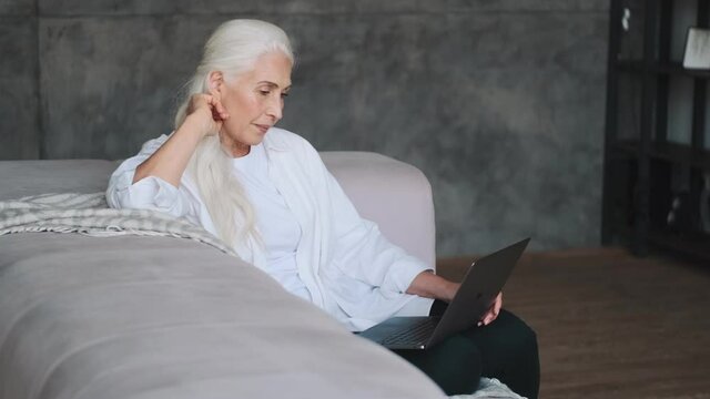 Pleased senior woman using laptop computer indoors at home