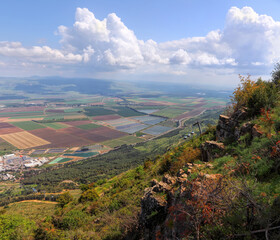 Obraz premium Panoramic view from Manara Cliff on Hula Valley. Kiryat Shmona city and beautiful farming landscape with agricultural land. Cableway cabins go up to the mountain. Upper Galilee. Northern Israel