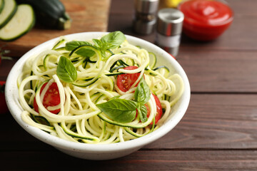 Delicious zucchini pasta with cherry tomatoes and basil in bowl on wooden table