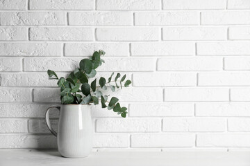 Beautiful eucalyptus branches in vase on white wooden table near brick wall. Space for text
