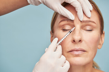 Cosmetologist giving injection in the glabellar wrinkle for mature woman