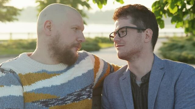 Portrait of two affectionate gay men look to each other in eyes. Homosexual couple dating in summer park. Intimate moment of love. LGBTQI, Pride Event, LGBT Pride Month, Gay Pride Symbol.