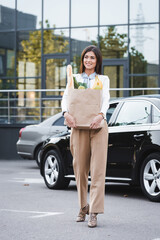  young woman holding shopping bag with food while walking along car parking