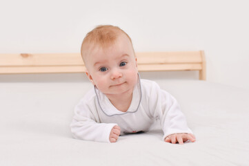 Adorable happy caucasian four-five months baby lying on stomach on bed, looking at camera