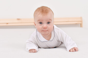 Naklejka premium Adorable happy caucasian four-five months baby lying on stomach on bed, looking at camera