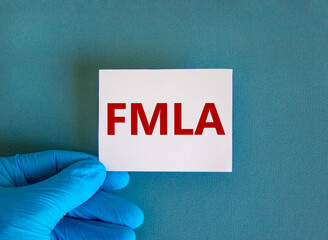 FMLA symbol. Hand in blue glove with white card. Concept words 'FMLA - family medical leave act'. Medical and FMLA concept. Copy space, beautiful blue background.