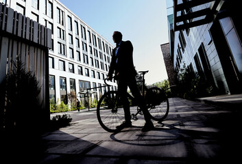 Silhouetted full length shot of mature businessman looking away while standing with his bicycle near modern office building outdoors