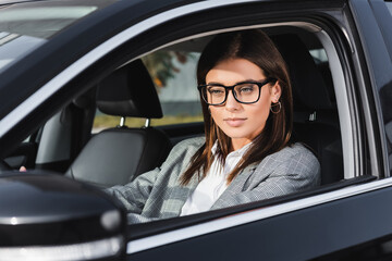  businesswoman in eyeglasses driving car on blurred foreground