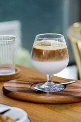 selective focus, wine glass of iced coffee two layers fresh milk and espresso short on wooden table at cafe. Refreshing summer drink concept