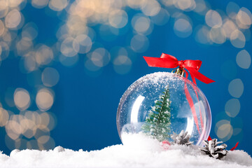 Decorative snow globe with red ribbon against blurred festive lights, closeup. Space for text