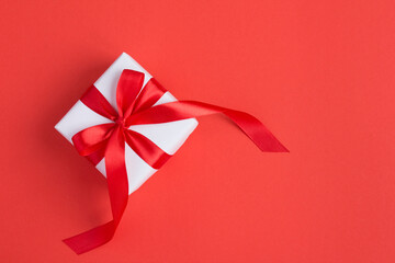 Top view of white gift box with red bow on the red background with copy space