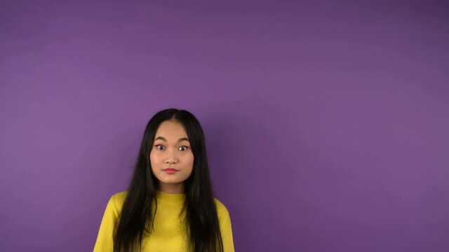 puzzled young asian woman in bright yellow sweater looks right. Free space for text and speech bubble. isolated purple background. 4K