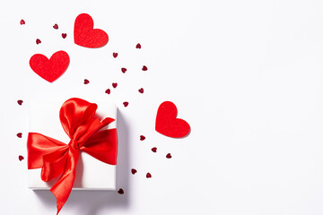 St. Valentine’s Day card concept. White gift box with big red bow and shining heart-shaped decorations on white background with copy space for your text.