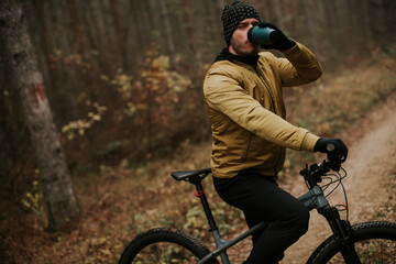 Young man taking a brake during biking through autumn forest