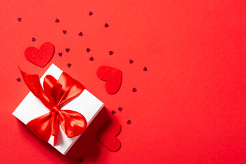 Bright festive composition with white gift box with big red bow and shining decorations on red background with copy space for your text. St. Valentine’s Day card concept.