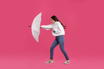 Woman with white umbrella caught in gust of wind on pink background