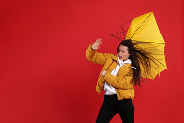 Emotional woman with umbrella caught in gust of wind on red background. Space for text