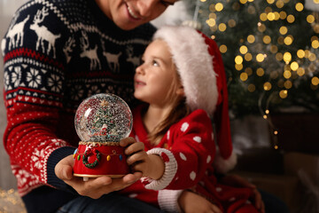 Father and daughter with snow globe near Christmas tree, focus on toy