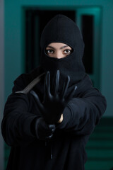 Thief broke into the apartment. House robbery by woman in a black jacket and black mask and crowbar. Burglar in a mask. Thief in a mask trying to break into other people's house	