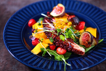 Octopus salad with mango and strawberries on a blue plate. Photos without people. Cooking concept.