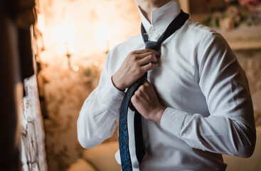 the groom straightens his tie, man in a tie, The morning of the groom, bridegroom's fees, fiance in shirt, in a blue tie