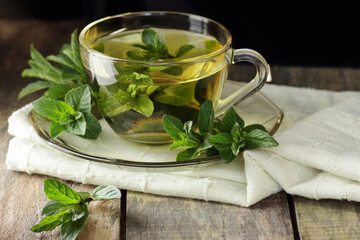 Pepper mint herbal leaf tea or gargling in a glass cup with herb leaves nearby on rustic wood, closeup, copy space, herbal drinks and naturopathy concept