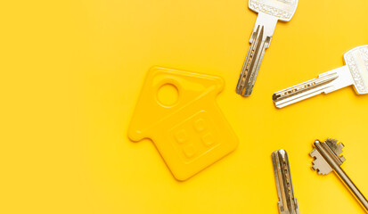 House symbol and metal keys on yellow background flat lay top view copy space. House door keys. Concept of buying home, apartment. Renting a house, real estate. Mortgage, credit, real estate insurance
