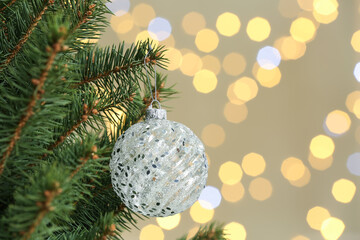 Holiday bauble hanging on Christmas tree against blurred lights. Space for text