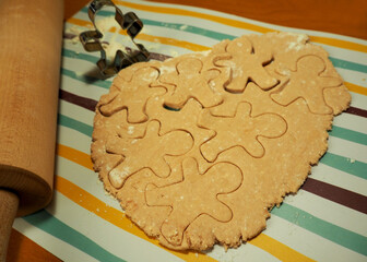 raw cookies made from cottage cheese and rice flour with date syrup in the form of a gingerbread man with a metal shape and a wooden rocking chair on the side during cooking at home side view