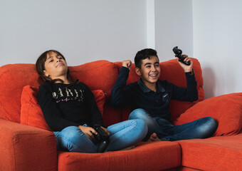 Two children sitting on the sofa at home playing video games.