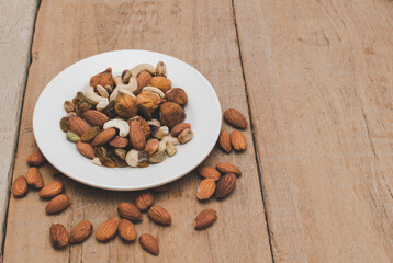 A variety of nuts  are in dish on wooden background at the center of the image, selective focus.