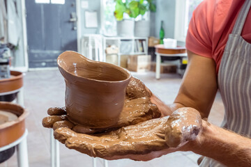 Male hand's holding a brown clay product created on a potter's wheel in a pottery workshop. Hobby concept, creative lesson and handicrafts.