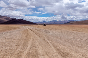 A car driving through the southwest of the altiplano in Bolivia in a cloudy day