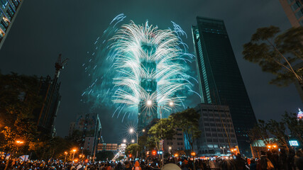 Taipei City Night landscape and Taipei 101 skyscraper is lit up by fireworks. People watching and taking photos and videos around buildings to celebrate the new year event.